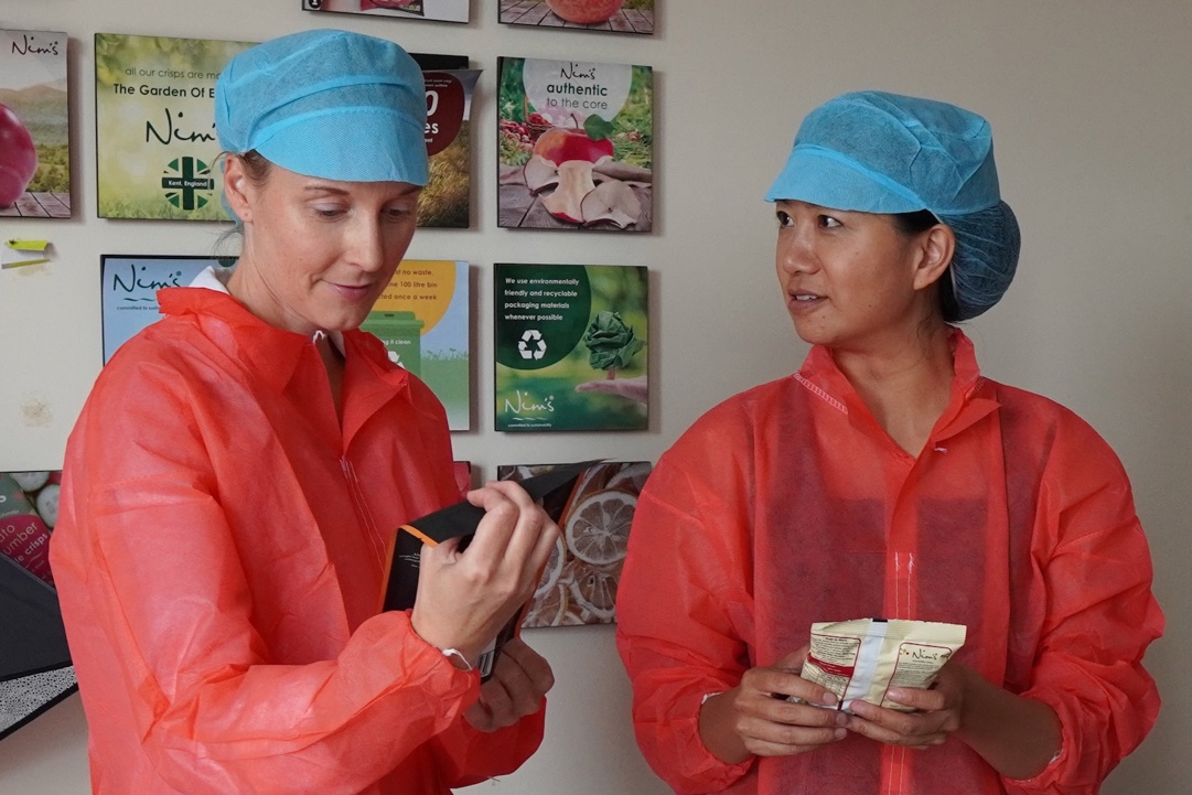 Women from the Food Accelerator cohort wearing orange raincoats and blue hairnets during their visit to Nim's Naturally factory