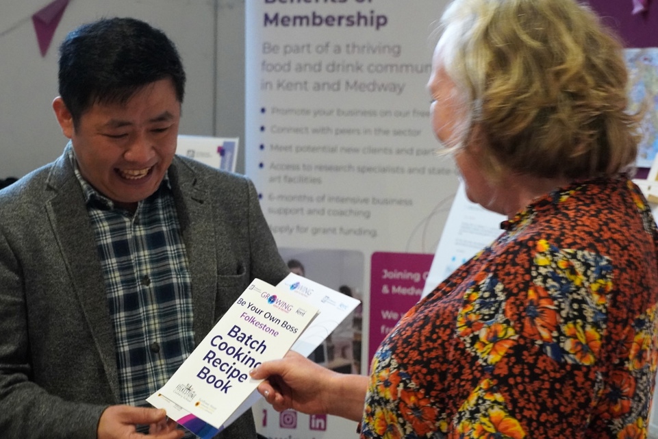 A woman presents a smiling man with a cetificate and recipe book.