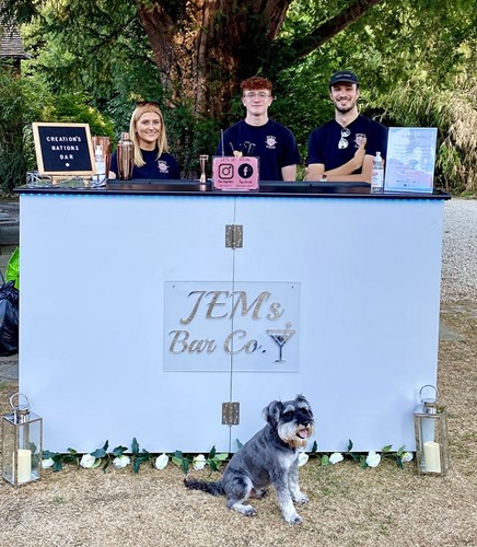JEMs Bar owners Emilie, James and friend ready to serve behind drinks bar, with grey dog