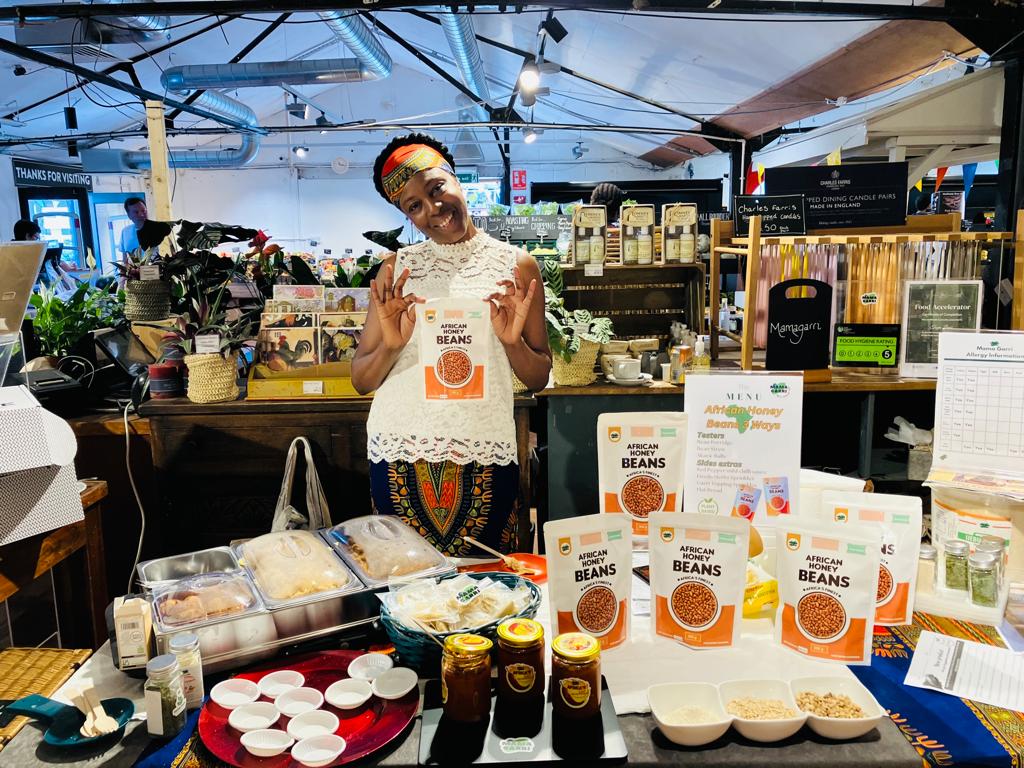 Sonya Okubule holding a packet of African honey beans behind her stall at Macknades